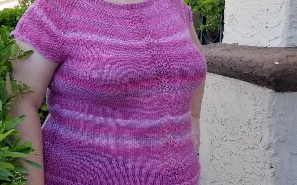 Stephanie wearing a knitted cap-sleeve raglan top in pink variegated yarn.