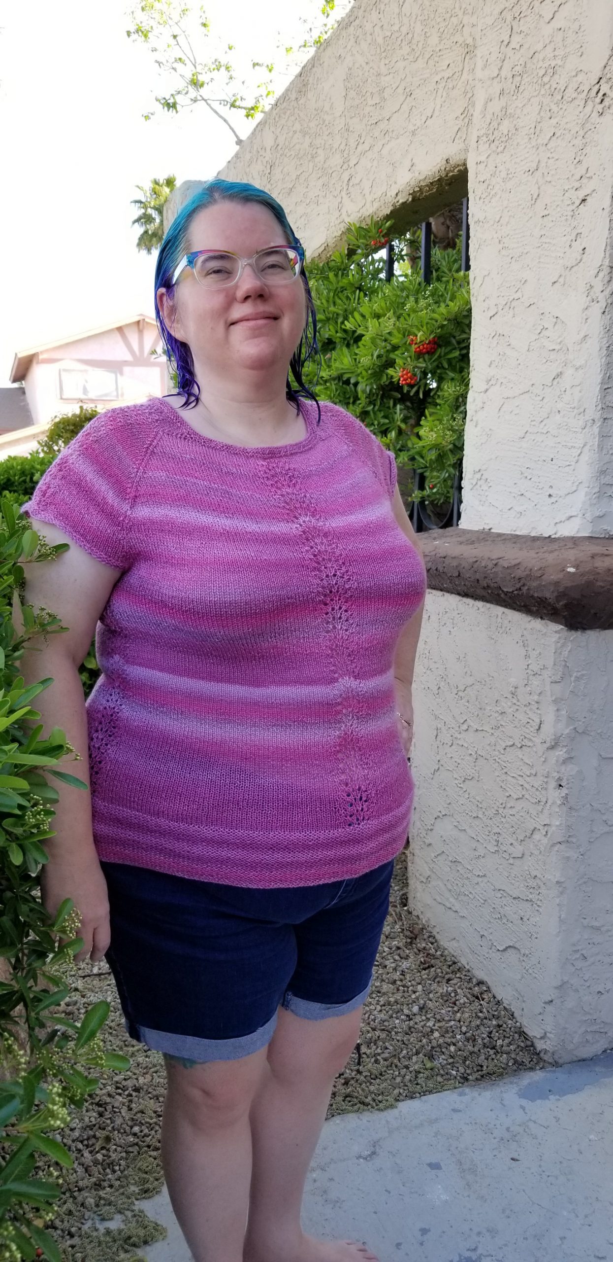 Stephanie wearing a knitted cap-sleeve raglan top in pink variegated yarn.