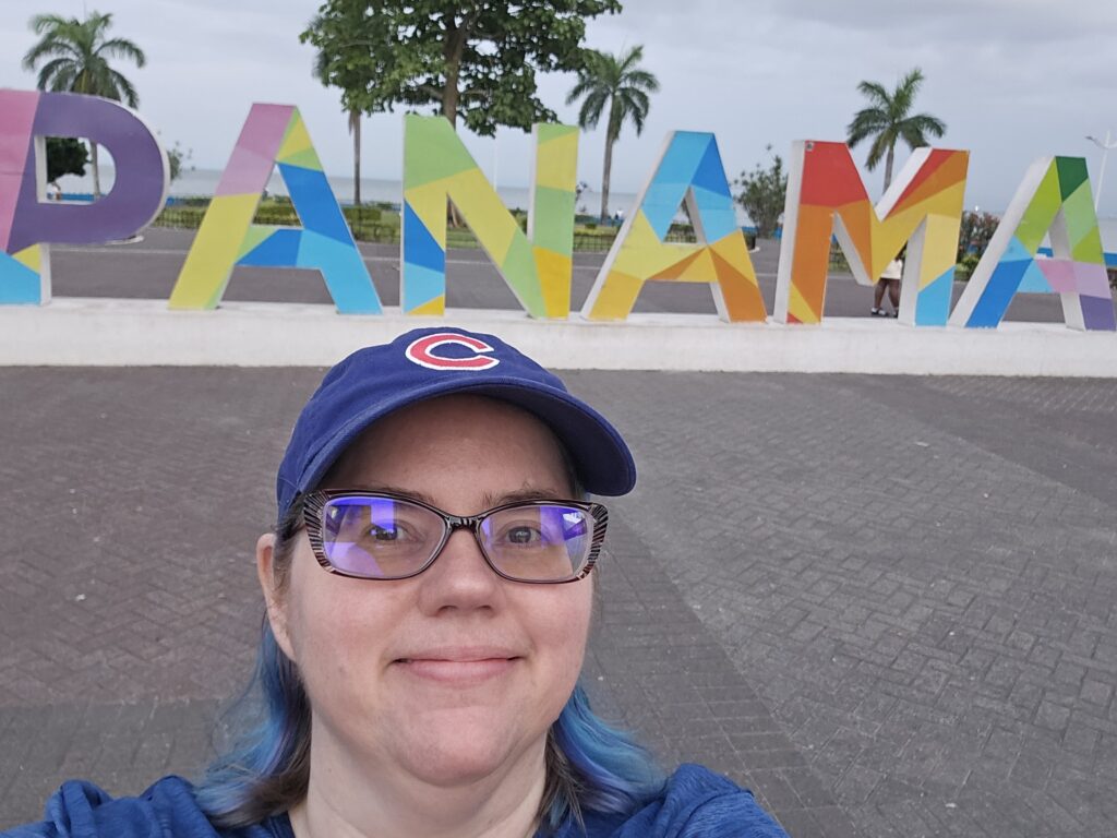 Stephanie, a blue-haired woman wearing glasses and a Chicago Cubs hat, is standing in front of a colorful sign that reads "PANAMA"