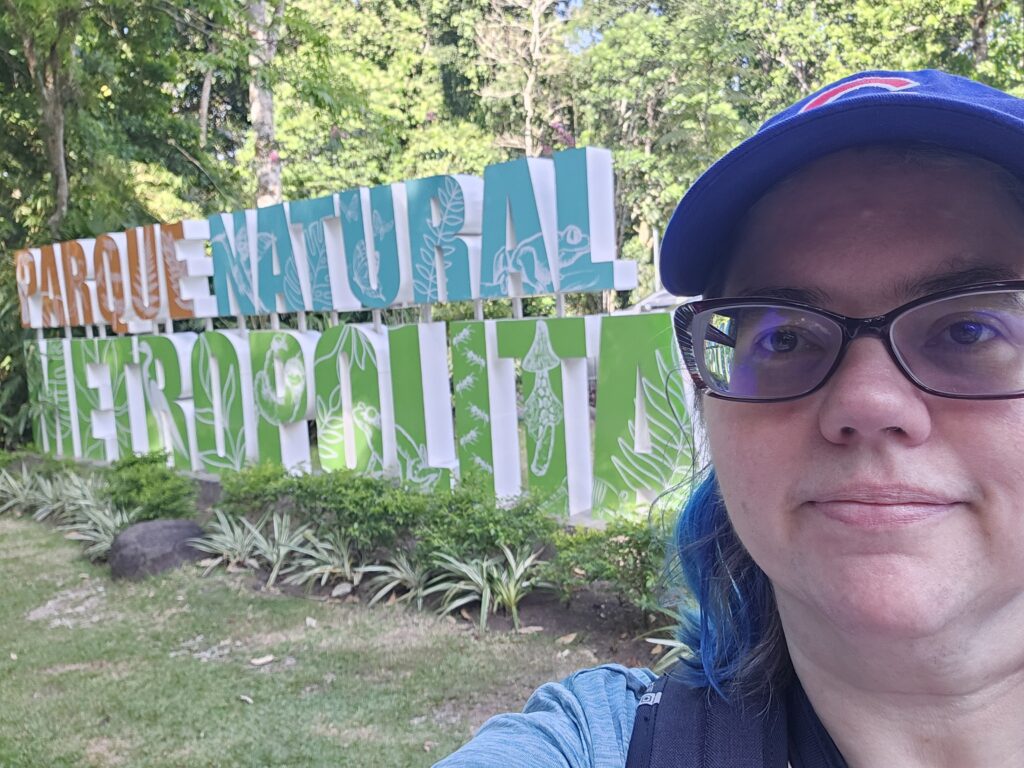 Stephanie, still wearing the Cubs hat, standing in front of an orange, blue, and green sign that says "Parque Natural Metropolitan"