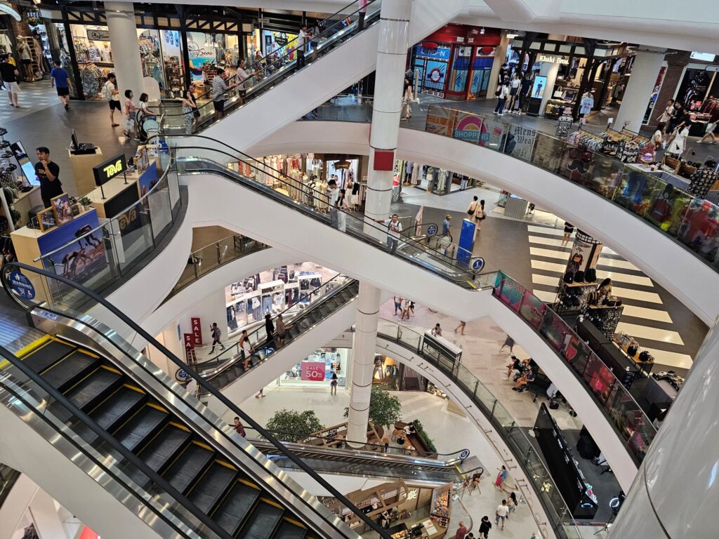 The inside of a multi-level mall, with numerous active shops and shoppers evident.