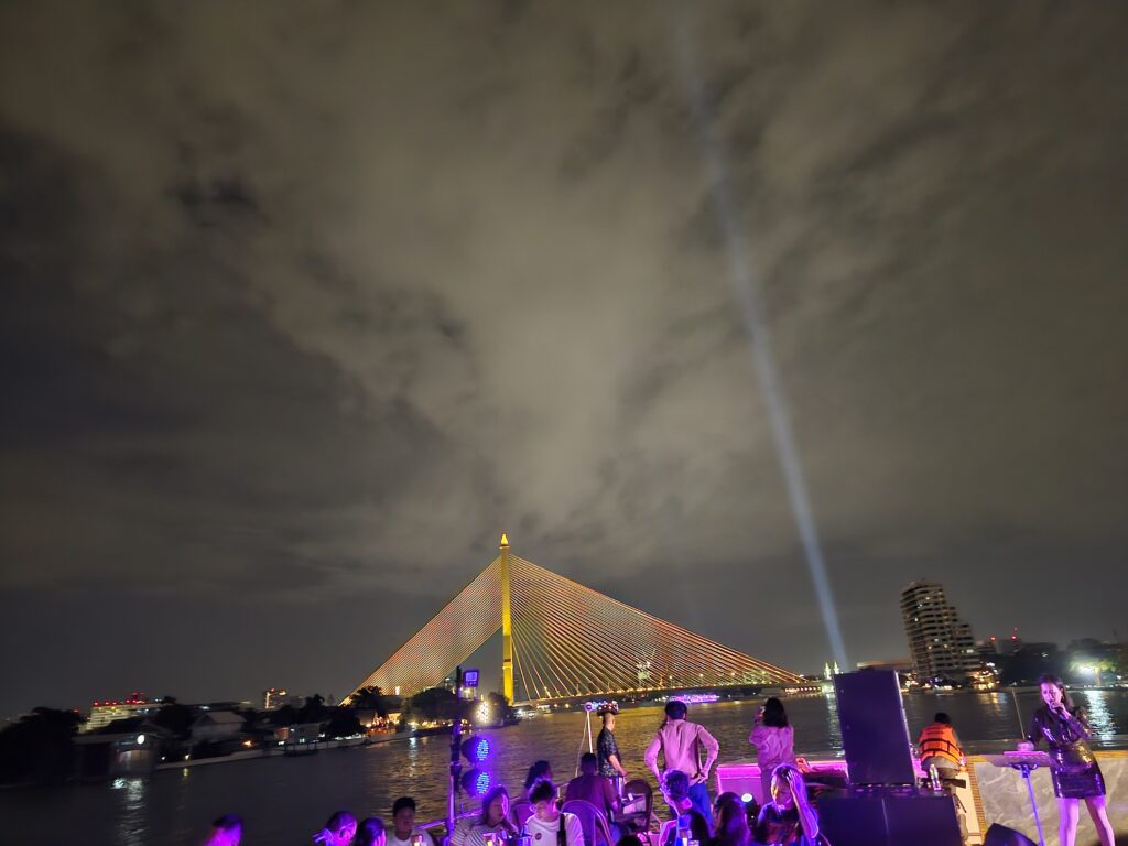 An asymmetrical bridge, the Rama VIII Bridge, lit up at night with a cloudy sky above.
