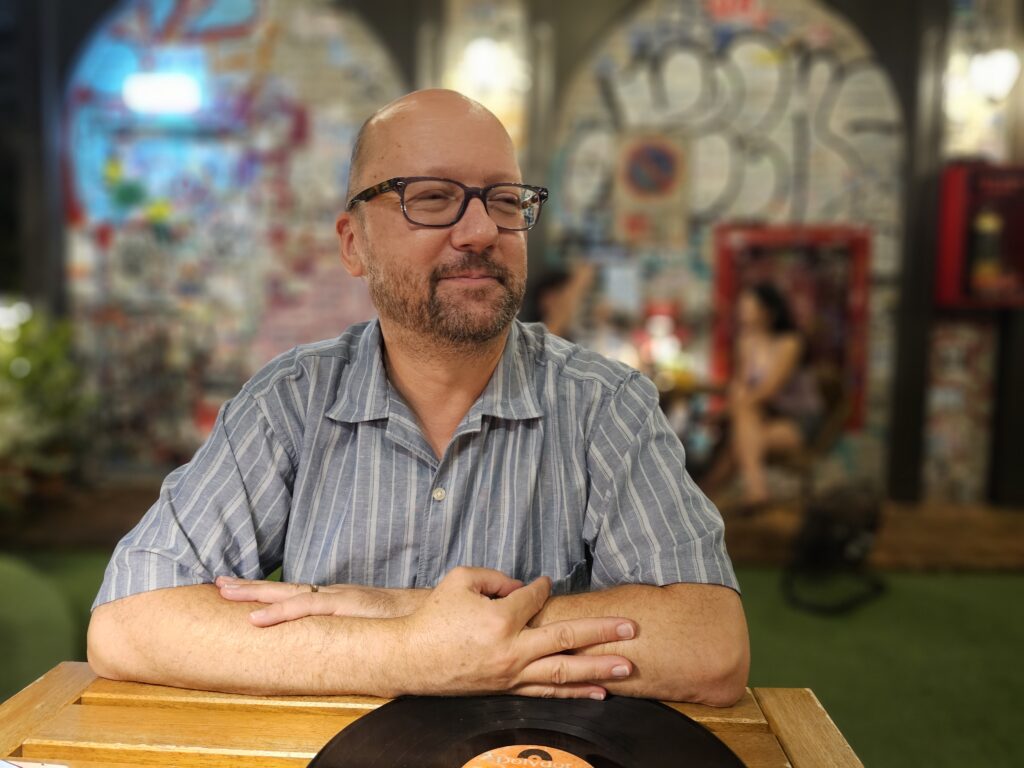 John, a middle-aged white man with glasses, shaved head, and beard, looking thoughtfully, at a restaurant
