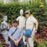 John and Stephanie, a white middle-aged couple, absolutely melting on the grounds of the Grand Palace, in front of a statue